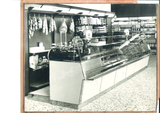 Negozio di alimentari con banco espositivo per prodotti freschi e scaffali in background.