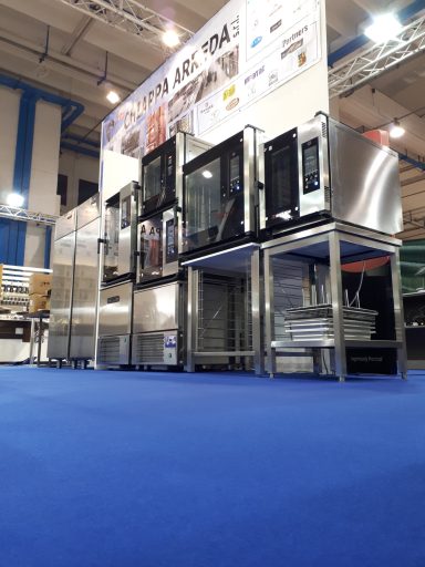 Attrezzature da cucina professionale in un ambiente espositivo con pavimento blu.