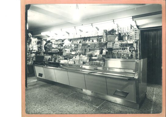 Banco refrigerato con cibi e bevande disposti ordinatamente. Ambiente interno vintage.