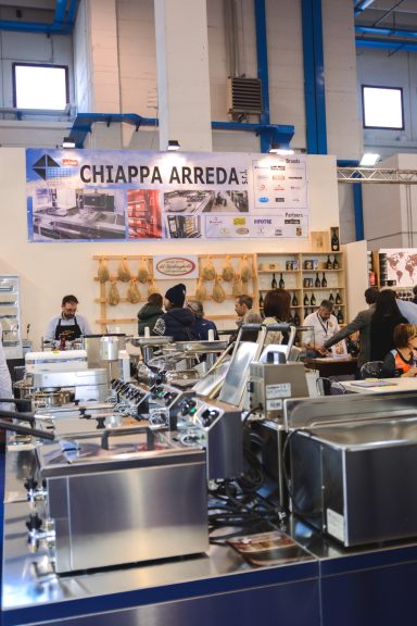 Stand di attrezzature da cucina con banconi e poster pubblicitari sullo sfondo.