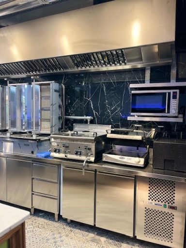 Modern commercial kitchen with stainless steel appliances and a black marble backsplash.