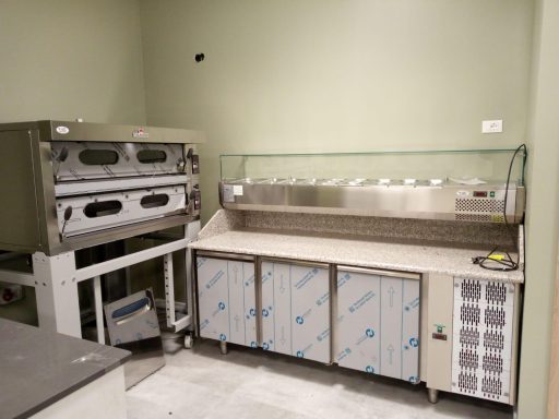 Attrezzatura da cucina con forni e banco frigo in un ambiente di ristorazione.